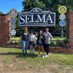Four people posing by Selma welcome sign.